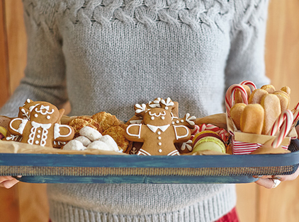 A person holding a tray full of Christmas cookies.